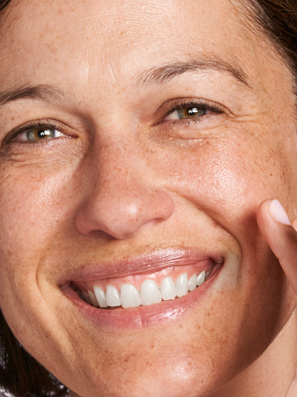 Bild som visar glad kvinna som applicerar hudvård.